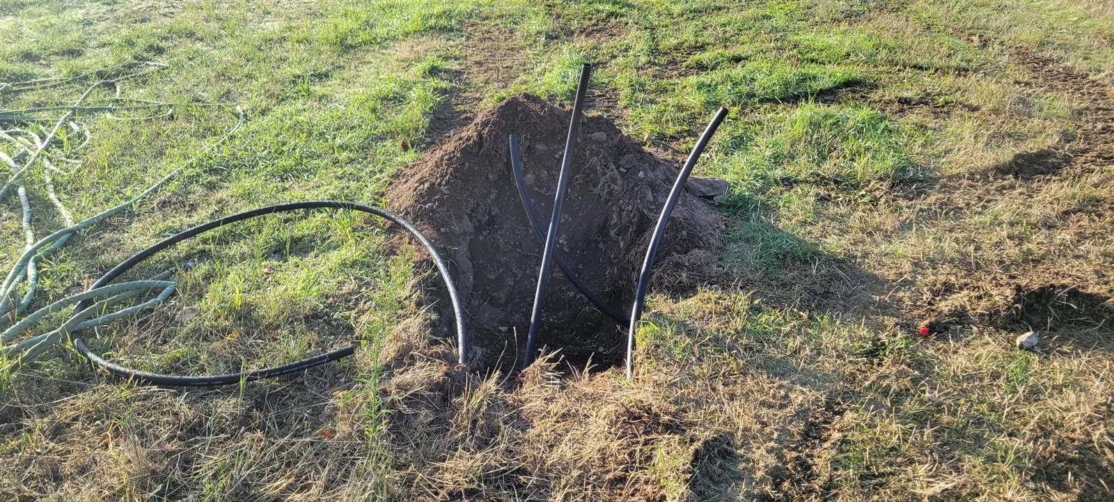 A sprinkler repair dig with the poly lines exposed in an open hole in the lawn