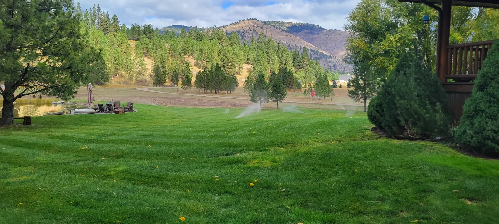 Sprinklers running across a wide green lawn with pine hills and mountains behind it in western Montana